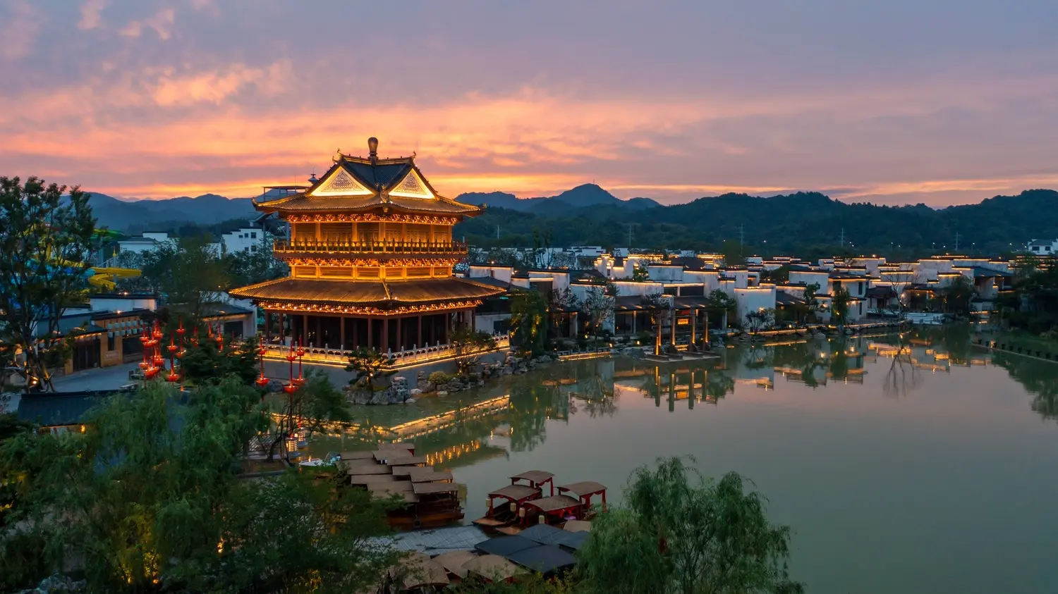 The stunning Wunvzhou Resort at sunset, featuring illuminated traditional Hui-style architecture reflected on tranquil waters in Jiangxi.