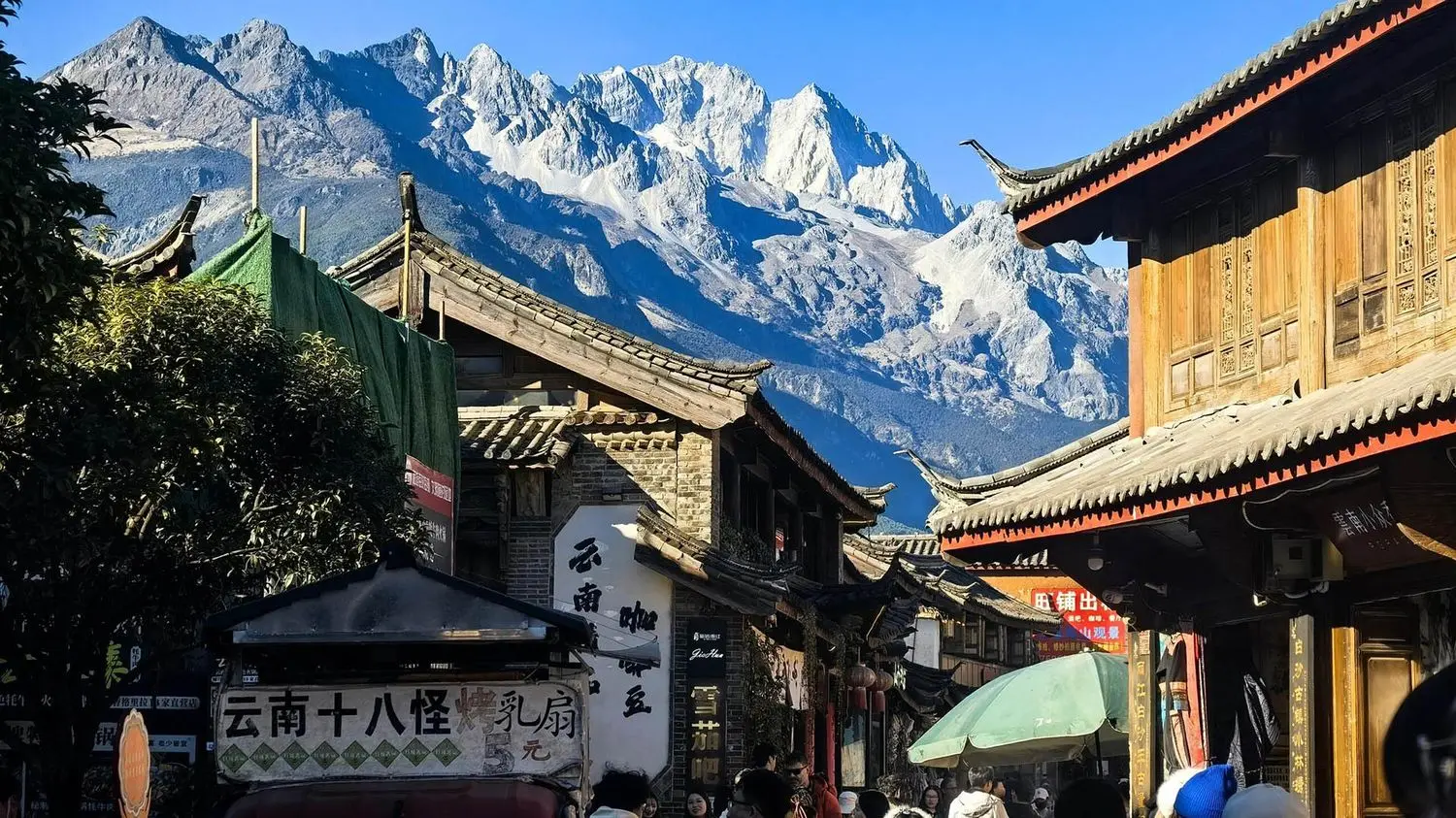 The peaceful streets of Baisha Ancient Town with the majestic Jade Dragon Snow Mountain in the background, showcasing Yunnan's Naxi heritage.
