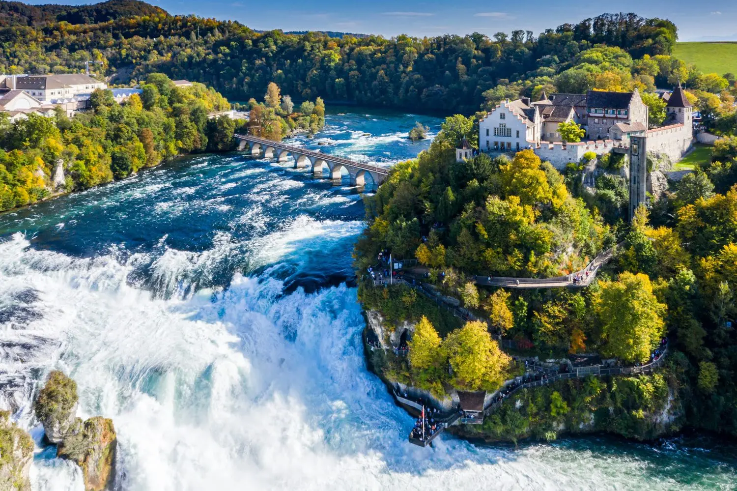 The magnificent Rhine Falls in Switzerland, Europe's largest waterfall, with powerful cascading waters surrounded by lush forests and historic landmarks near Schaffhausen.