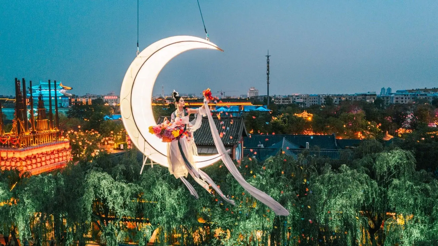 Visitors enjoying the iconic moon swing at Qingming Riverside Landscape Garden in Kaifeng, Henan, China, surrounded by beautiful evening lights, Song Dynasty architecture, and immersive cultural attractions.