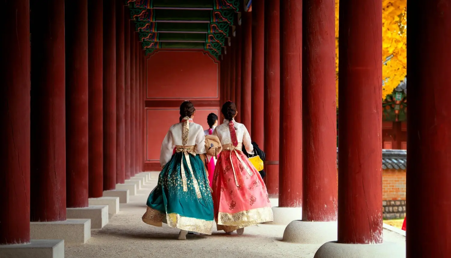 Visitors wearing traditional Korean hanbok walking through the red-pillared corridor of Gyeongbokgung Palace in Seoul, showcasing Korea's rich cultural heritage and historic royal architecture.
