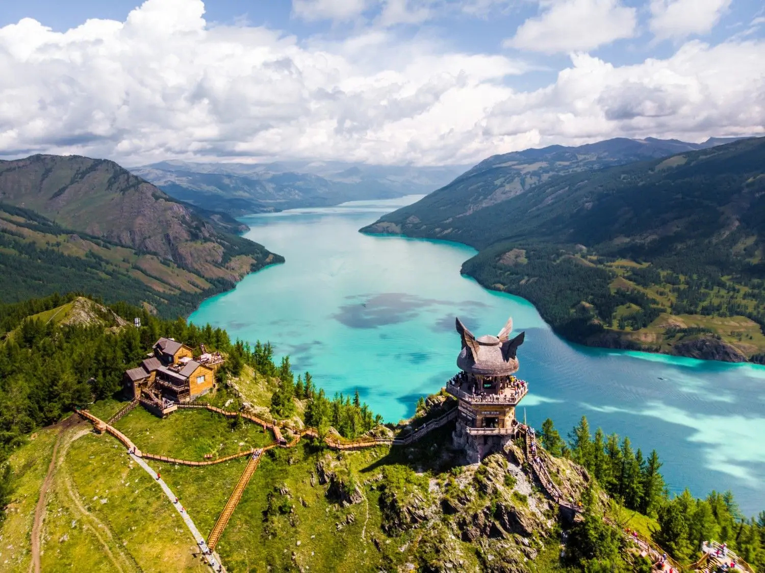 Kanas Lake in Xinjiang, China, featuring crystal-clear turquoise waters, breathtaking alpine mountains, and panoramic views from Guanyu Pavilion, one of Northern Xinjiang's most spectacular natural attractions.